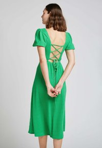 Robe midi verte avec des manches bouffantes, en tissu texturé, dos ouvert avec des bretelles croisées et un détail de lien à la taille.
