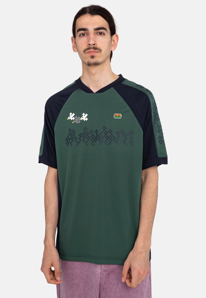 Jersey de manga corta verde y marino con cuello en V, que presenta patrones pixelados y un pequeño logo en el pecho. Tela suave y transpirable.