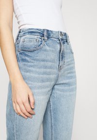 Vaaleansiniset farkut, joissa on hieman haalistunut pinta, viisi taskua, näkyvät saumat ja korkea vyötärö. Sileä rakenne ja suorat lahkeet.