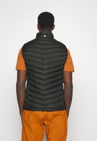 Czarna, bezrękawnikowa kurtka puchowa w wzór chevron, z wysokim kołnierzem i zapięciem na zamek. W połączeniu z pomarańczową koszulą z krótkim rękawem.