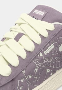 Sneaker in pelle scamosciata viola con lacci bianchi, caratterizzato da un design grafico di gatti sul lato. Logo sulla linguetta. Suola in gomma texturizzata.