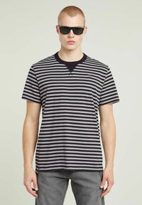 Czarny i szary T-shirt w paski z okrągłym dekoltem i kr ótkimi rękawami, wykonany z miękkiego materiału, noszony w ciemnych okularach.