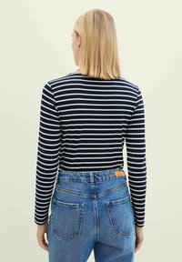 Marineblaue und weiße gestreifte Langarmbluse, kombiniert mit hochgeschnittenen blauen Jeans, die ein Etikett am hinteren Bund und zwei Gesäßtaschen aufweisen.