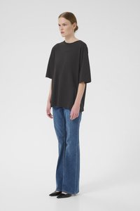 Zwart T-shirt met korte mouwen en een relaxte pasvorm, gecombineerd met blauwe flared jeans en zwarte puntige schoenen. Minimalistisch ontwerp zonder zichtbare patronen.