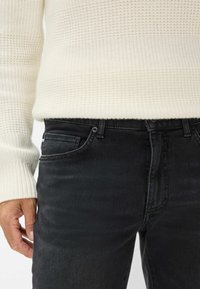 Maglione bianco a maglia spessa con motivo testurizzato abbinato a jeans in denim neri con tasche frontali e leggero sbiadimento.