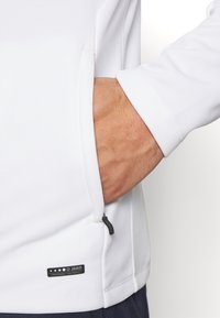 Witte lange mouwen top met een zijsac en een contrasterende zwarte rits. Voorzien van een zichtbaar merklabel op de zoom. Vlotte textuur.