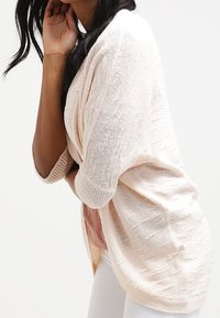 Světle růžový, strukturovaný oversized kardigan s širokými rukávy a volným střihem. Disponuje otevřeným předním designem a jemným vzorem na látce.