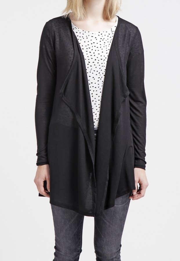 Cardigan nero a maniche lunghe con apertura frontale e design drappeggiato, indossato sopra una camicia bianca con piccoli triangoli neri, abbinato a jeans grigi.