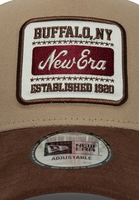 Καφέ καπέλο τύπου ταν με καφέ λεπτομέρειες, που διαθέτει ορθογώνιο λευκό σημείο με κόκκινο κείμενο «Buffalo, NY», «New Era» και «Established 1920». Ρυθμιζόμενο μέγεθος.
