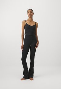 Top corto negro sin mangas con tirantes finos combinado con leggings ajustados negros de tiro alto y acampanados. Textura suave, diseño minimalista.
