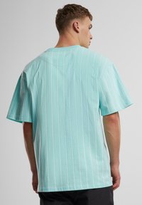 T-shirt en coton turquoise avec des rayures verticales blanches, à manches courtes et à coupe décontractée, vue de dos.