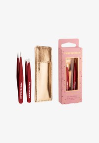 Röda metallpincetter med spetsiga och lutande spetsar, förvarade i ett fodral av guldimitationläder och förpackade i en rosa ask med blomsterdesign.