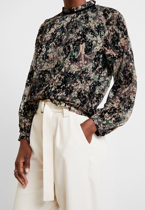 Bloemmotief sheer blouse met lange mouwen, in zwart en groen tinten, met een gerimpelde halslijn, gecombineerd met hooggewaadde crèmekleurige broek.