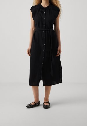 Czarna sukienka do kolan z przodem na guziki, krótkimi rękawkami typu cap i paskiem w talii. Wykonana z teksturowanej tkaniny z pionowymi plisami. Czarne baleriny z ćwiekami.