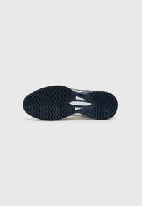 Vit sneakersula med en texturerad svart gummiyttersula som har zigzagmönster och ett centralt utskärning; Fila-logotyp präglad.