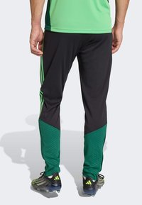 Črne športne hlače z zelenimi poudarki, s teksturiranim vzorcem na spodnjem delu noge in tremi zelenimi črtami ob straneh.