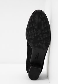 Chaussure noire en suède avec une semelle en caoutchouc texturé présentant un motif de grip ; marque Gabor visible, prise en angle sur un fond clair.