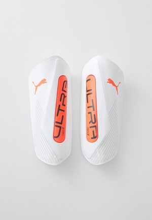 Puma ULTRA Schienbeinschoner aus weißem Kunststoff mit orangenen Akzenten. Verfügt über ein strukturiertes Design und eine auffällige "ULTRA TWIST"-Branding.