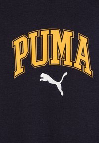 PUMA t-skjorte har fet gult skrift på marineblått stoff, med en hvit silhuett av en sprangende katt-logo. Smooth tekstur, rund halsdesign.