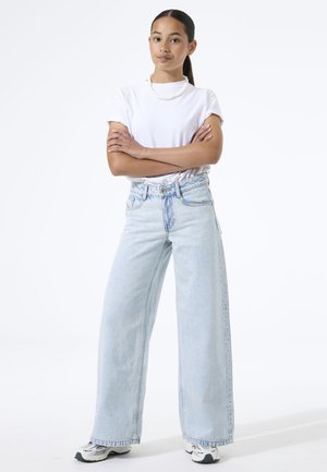 Jeans de pierna ancha y cintura alta en azul claro con un acabado desgastado y trabillas para cinturón, combinados con una camiseta blanca ajustada y zapatillas casuales.