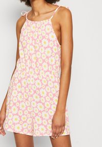 Růžový overal bez rukávů s žlutým a bílým květinovým vzorem. Má zavazovací ramínka a přiléhavý pas, vyrobený z lehkého materiálu.