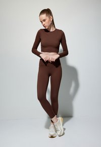 Brun langærmet crop top og matchende leggings lavet af strækbart stof, med en glat overflade og tætsiddende silhuet, parret med lette sneakers.