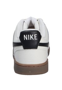 Zapatilla blanca con parte superior de cuero texturizado, acento negro en el talón y suela de goma. Presenta el logotipo de Nike en la parte trasera.