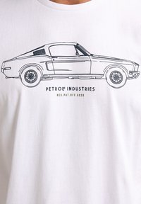 Hvid t-shirt med en sort stregtegning af en klassisk bil, mærket "PETROL INDUSTRIES", med en glat bomuldsstruktur.