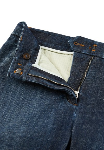Pantalones de mezclilla azul oscuro con cremallera; cuenta con un cierre de botón y costuras en color marrón en la cintura y los bolsillos. Forro de algodón blanco visible.