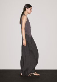 Modèle portant un débardeur gris texturé et un pantalon palazzo noir à rayures lâches avec une jambe large, associé à des sandales plates.