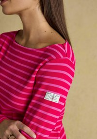 Vaaleanpunainen ja fuksia raidallinen pitkähihaisuus toppi, jossa on veneenäköinen kaula-aukko ja tarralapuke hihassa. Materiaali näyttää pehmeältä ja tekstuuriltaan mielenkiintoiselta.