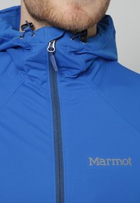 Veste imperméable bleue avec un col montant et une capuche ajustable, équipée d'une fermeture éclair frontale et du logo "Marmot" en gris clair.