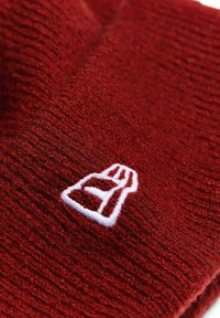 Berretto lavorato a maglia rosso con un motivo testurizzato. Presenta un logo ricamato bianco sul davanti. Materiale morbido, design caldo adatto per il freddo.