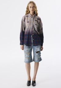 Geruit overhemd in verschillende pastel- en donkere kleuren; met scheuren. Gecombineerd met versleten denim shorts, middellang, ruime pasvorm en rafelige randen.