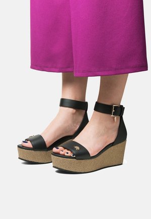 Sandali platform neri con base intrecciata testurizzata, caratterizzati da una cinghia alla caviglia e un accento dorato. Il design open toe mette in risalto unghie dei piedi curate.