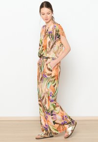 Jumpsuit s cvetličnim vzorcem v oranžnih in zelenih odtenkih, kratkimi rokavi, ohlapnega kroja, z stranskimi žepi in sijočimi kovinskimi sandali.
