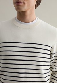 Cream knit sweater with navy horizontal stripes, round neckline, and ribbed cuffs. Soft texture and relaxed fit.
