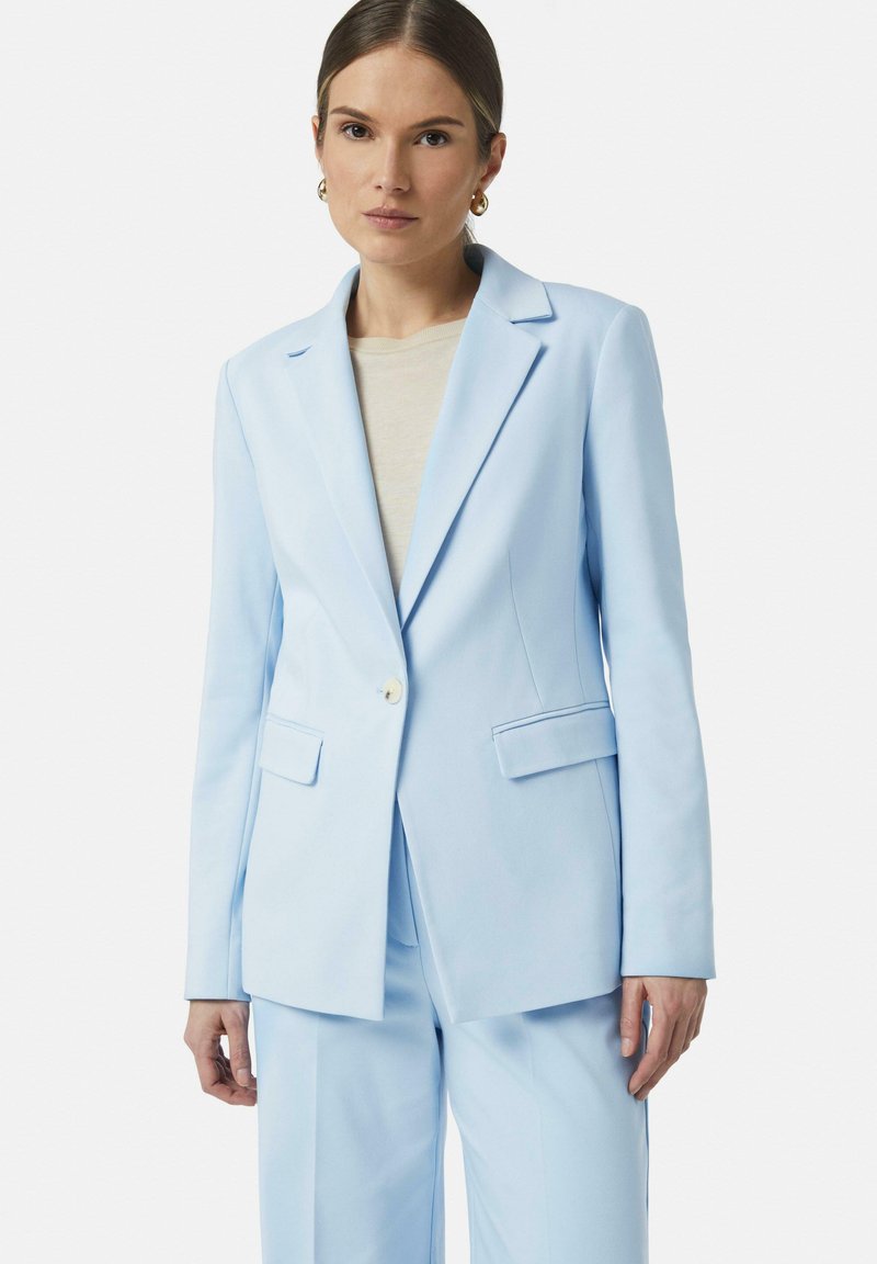 Lichtblauwe op maat gemaakte blazer met reverskraag, enkelknopsluiting en twee voorzakken. Draag het over een beige top, met een soepele textuur.