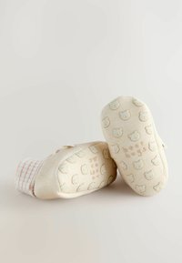 Chaussons pour bébés en tissu doux, beige avec des motifs d'ours, dotés d'une semelle texturée et d'un accent rayé. Fermeture à bouton sur le côté pour un enfilage facile.