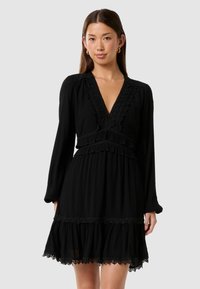 Abito nero con scollo a V profondo, maniche lunghe e ruffles sovrapposti. Presenta dettagli in pizzo all'collo e all'orlo. Silhouette fluida.