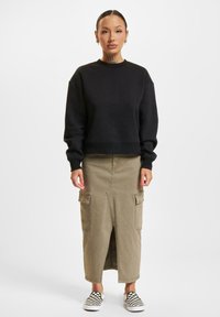 Sort cropped sweatshirt, olivgrønn cargo-skjørt med frontslitt og sidelommer, kombinert med svart og hvit rutete slip-on sko.