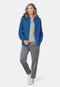 Blauwe fleece jas met een knoopsluiting aan de voorkant, een grijze gebreide top eronder, grijze suède-achtige broek en witte sneakers. Casual outfit.