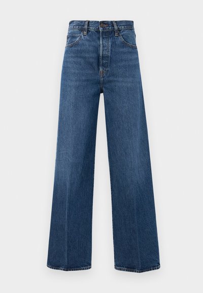 Jean bleu à jambes larges en denim avec taille haute, poches avant et couture contrastante. Le tissu a une texture lisse.