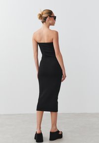 Juoda be petnešėlių midi suknelė, prigludusi silueto, pagaminta iš lygaus audinio, derinama su platforminiais sandalais ir elegantiškais akinių nuo saulės.