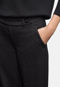Pantalons noirs avec un subtil éclat métallique, dotés d'une taille standard, de poches avant et d'un design épuré à jambes droites.