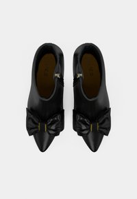 Zwarte leren enkellaarsjes met spitse neuzen, voorzien van oversized zwarte satijnen strikken aan de voorkant en gouden hardwareaccenten.