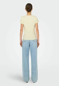 Gul og hvid stribet kortærmet skjorte parret med lyseblå brede jeans, set fra ryggen. Blødt stof og klassisk pasform.