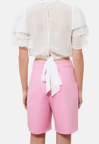 Top in tessuto trasparente a pois bianchi con maniche a sbuffo e legatura sul retro, abbinato a pantaloni corti fucsia su misura. Texture morbida e design aderente.