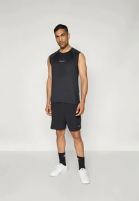 Svart ärmlös sporttopp och shorts, båda med en logotyp, tillsammans med vita sneakers. Ren, enkel design, lämplig för sport.