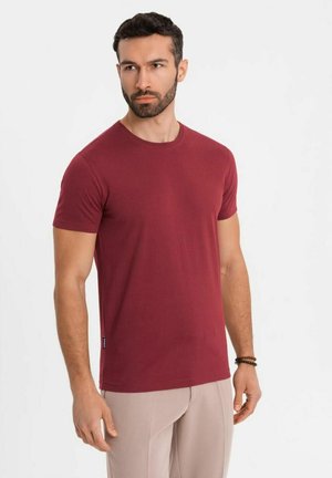 Burgundy crew-neck t-shirt with short sleeves, made of soft fabric; paired with light-colored trousers, featuring a small brand tag.